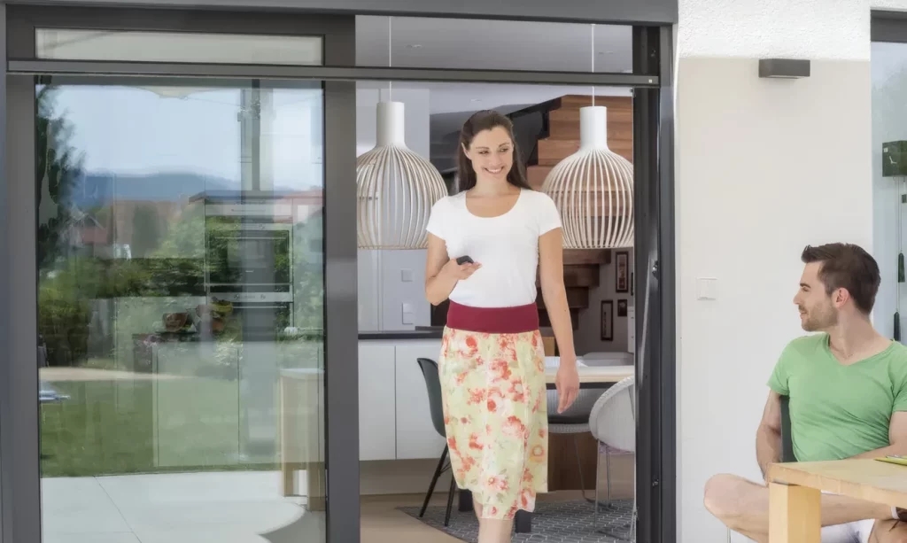 Eine junge Frau und ein junger Mann vor einem Insektenschutz-Elektro-Rollo vor ihrer Terrasse, die Frau hält die Fernbedienung für das Elektro-Rollo in der Hand