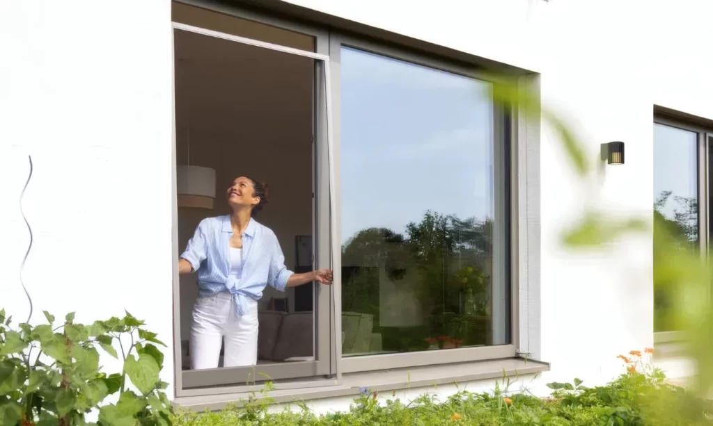 Frau hält Insektenschutz-Spannrahmen an das Fenster an